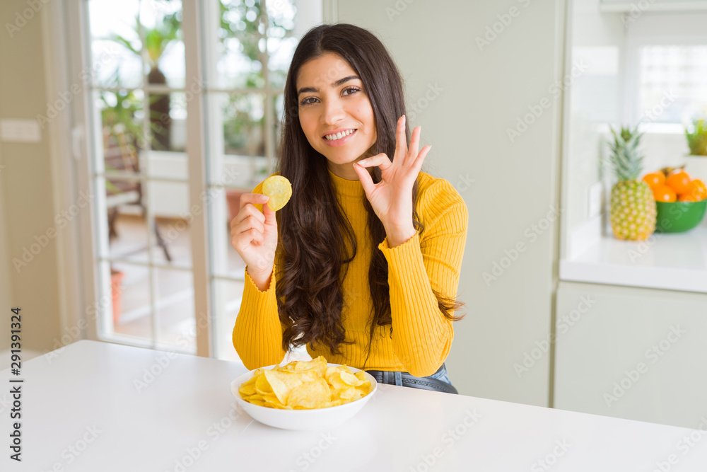 Young woman eating fastfood potato chips doing ok sign with fingers, excellent symbol Young woman eating fastfood potato chips doing ok sign with fingers, excellent symbol