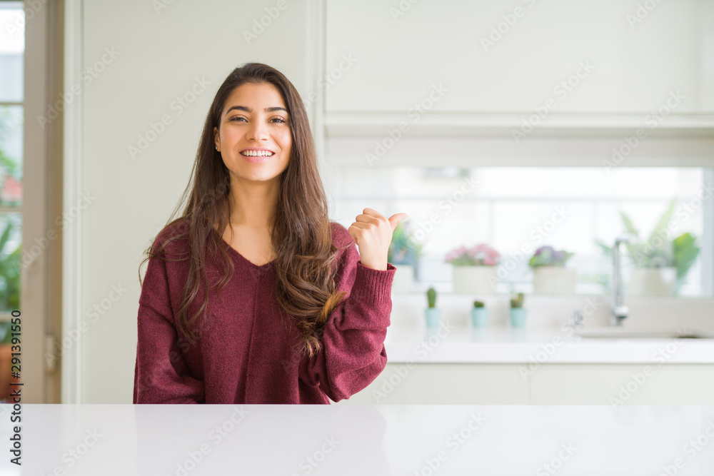 Young beautiful woman at home smiling with happy face looking and pointing to the side with thumb up. Young beautiful woman at home smiling with happy face looking and pointing to the side with thumb up.