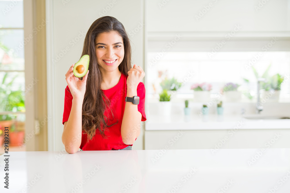 Young woman eating healthy avocado screaming proud and celebrating victory and success very excited, cheering emotion