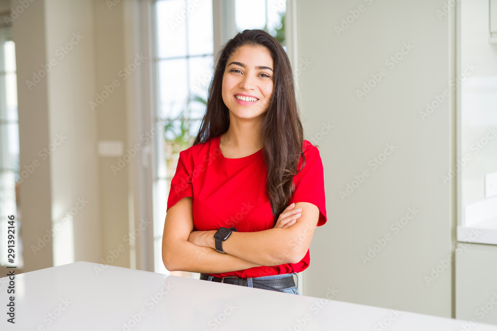 Young beautiful woman at home on white table happy face smiling with crossed arms looking at the camera. Positive person. Young beautiful woman at home on white table happy face smiling with crossed arms looking at the camera. Positive person.