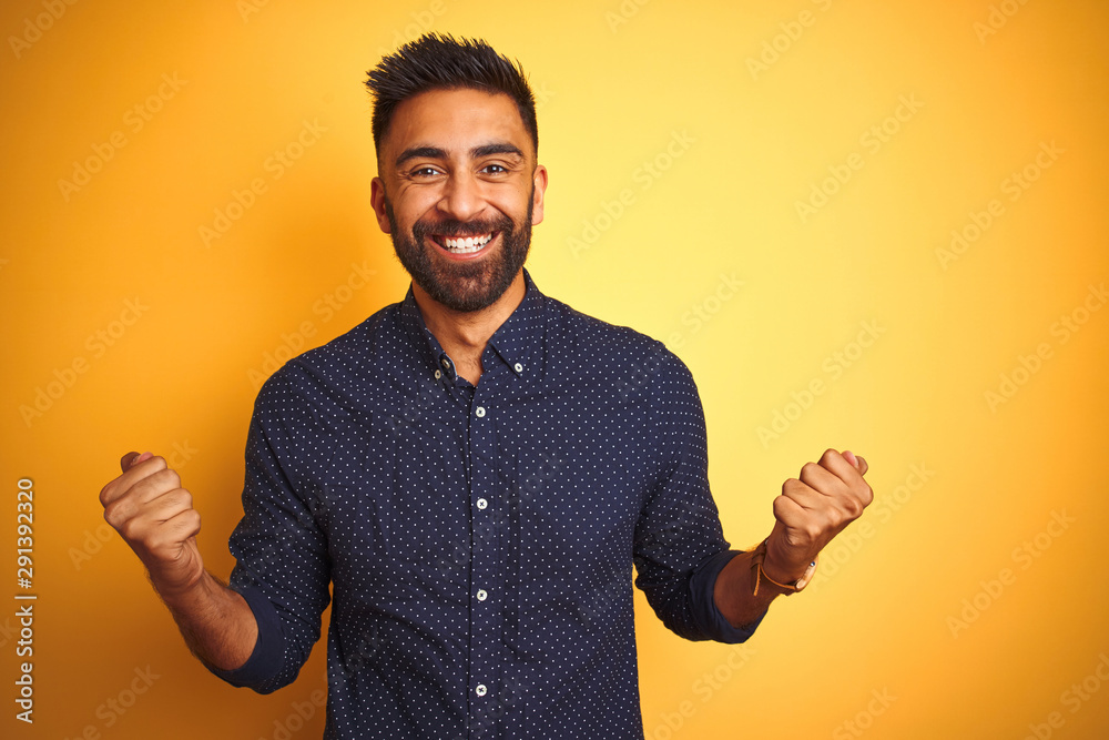 Young handsome indian businessman wearing shirt over isolated yellow background celebrating surprised and amazed for success with arms raised and open eyes. Winner concept. - obrazy, fototapety, plakaty 