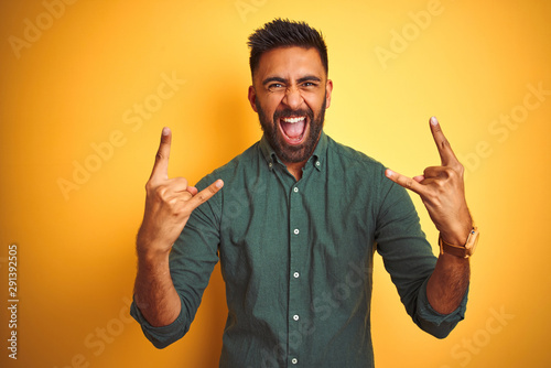 Young indian businessman wearing elegant shirt standing over isolated white background shouting with crazy expression doing rock symbol with hands up. Music star. Heavy concept.