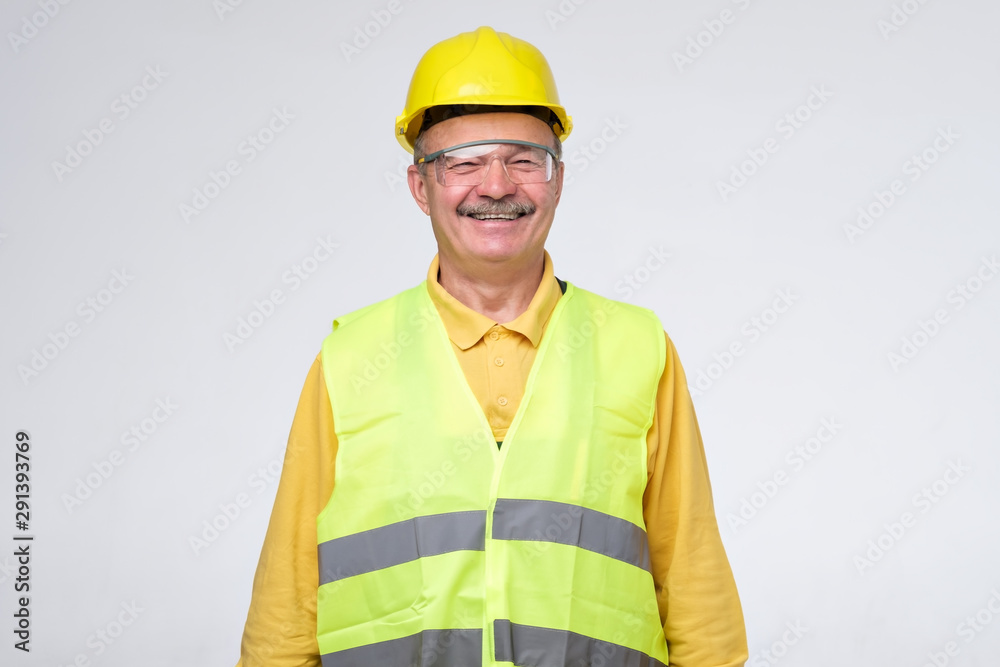 Senior hispanic construction worker in hard hat smiling on gray background. Positive facial human emotion. Senior hispanic construction worker in hard hat smiling on gray background. Positive facial human emotion.