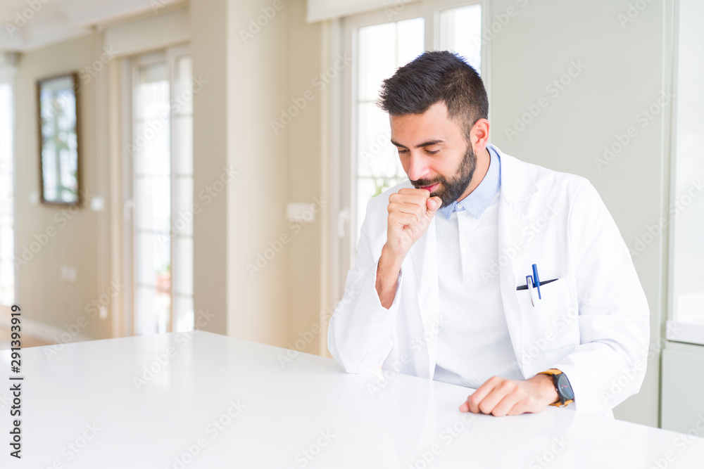Handsome hispanic doctor or therapist man wearing medical coat at the clinic feeling unwell and coughing as symptom for cold or bronchitis. Healthcare concept.