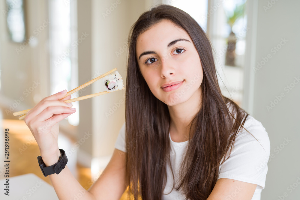 Beautiful young woman eating asian sushi using chopsticks with a confident expression on smart face thinking serious Beautiful young woman eating asian sushi using chopsticks with a confident expression on smart face thinking serious