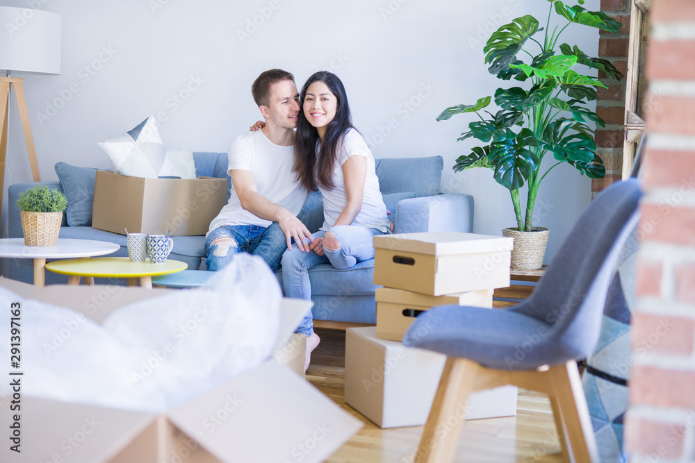 Young beautiful couple sitting on the sofa drinking coffee at new home around cardboard boxes Young beautiful couple sitting on the sofa drinking coffee at new home around cardboard boxes
