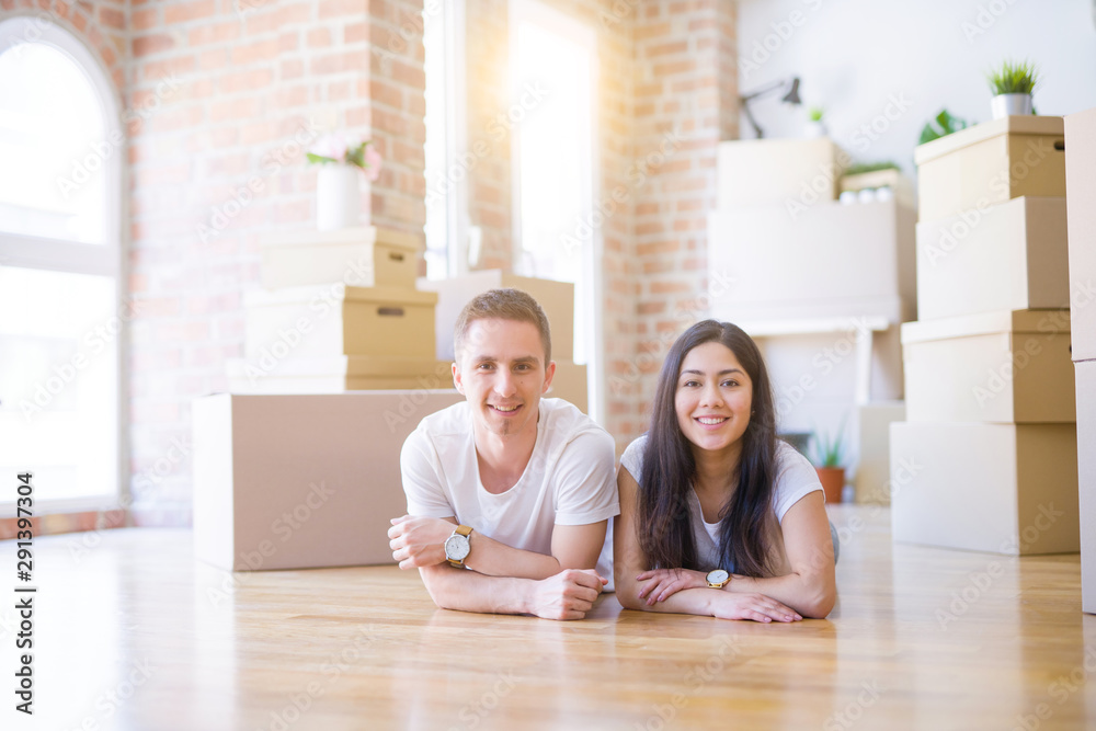 Young beautiful couple lying down at new home around cardboard boxes Young beautiful couple lying down at new home around cardboard boxes