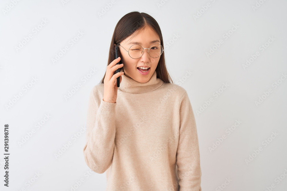 Young chinese woman talking on the smartphone over isolated white background winking looking at the camera with sexy expression, cheerful and happy face. Young chinese woman talking on the smartphone over isolated white background winking looking at the camera with sexy expression, cheerful and happy face.