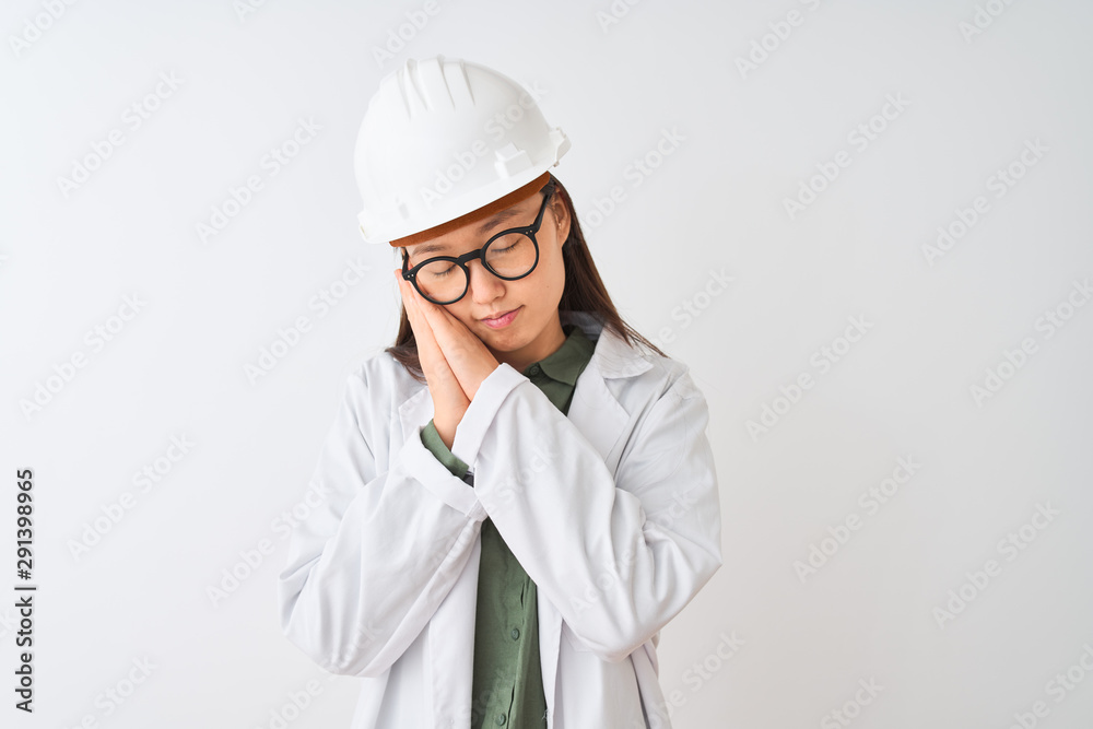 Young chinese engineer woman wearing coat helmet glasses over isolated white background sleeping tired dreaming and posing with hands together while smiling with closed eyes. Young chinese engineer woman wearing coat helmet glasses over isolated white background sleeping tired dreaming and posing with hands together while smiling with closed eyes.