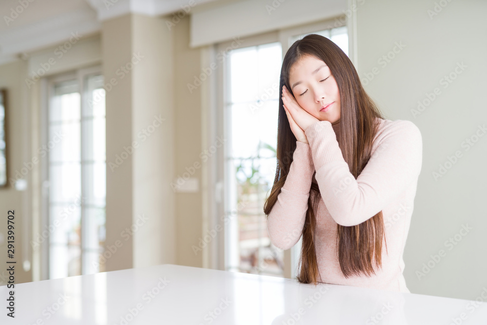 Beautiful Asian woman wearing casual sweater on white table sleeping tired dreaming and posing with hands together while smiling with closed eyes. Beautiful Asian woman wearing casual sweater on white table sleeping tired dreaming and posing with hands together while smiling with closed eyes.
