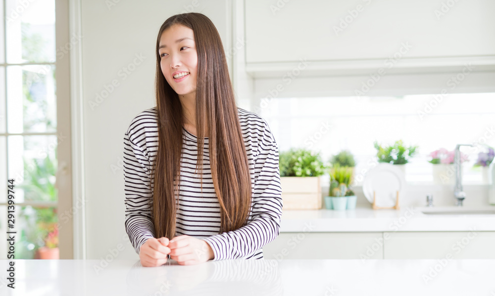 Beautiful Asian woman wearing stripes sweater looking away to side with smile on face, natural expression. Laughing confident.