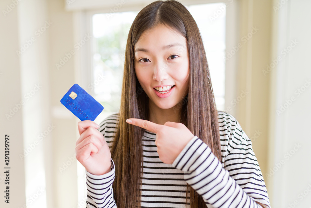 Beautiful Asian woman holding credit card very happy pointing with hand and finger Beautiful Asian woman holding credit card very happy pointing with hand and finger
