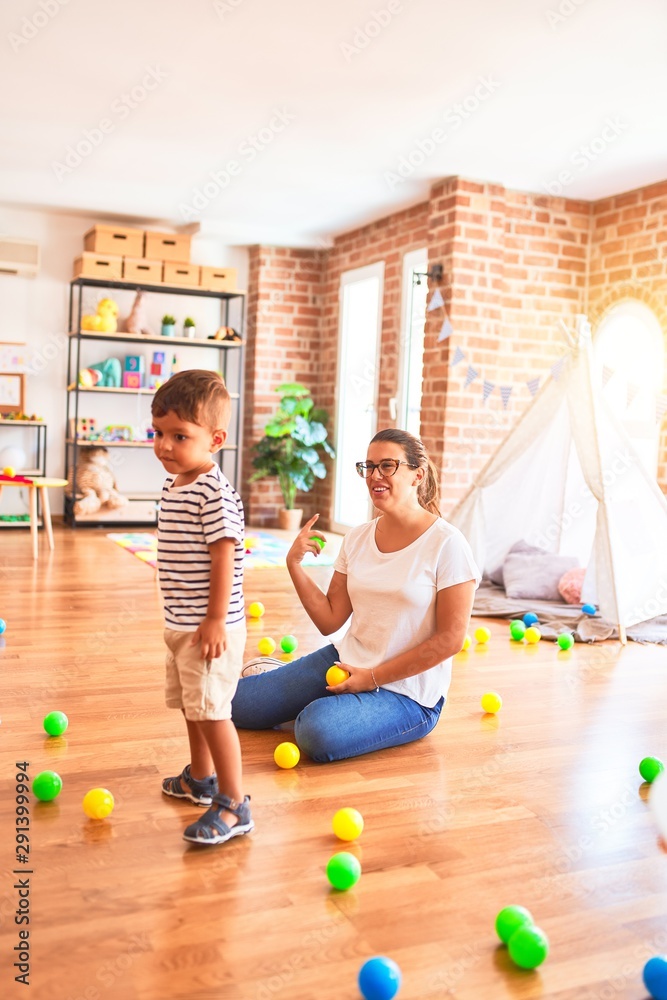 Fototapeta premium Beautiful teacher and toddler boy playing with colored small balls at kindergarten