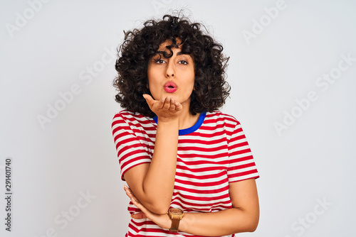 Young arab woman with curly hair wearing striped t-shirt over isolated white background looking at the camera blowing a kiss with hand on air being lovely and sexy. Love expression. © Krakenimages.com
