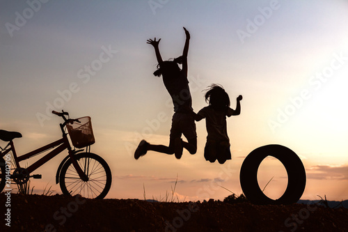 Silhouette of happy children jumping playing on mountain at sunset sky background