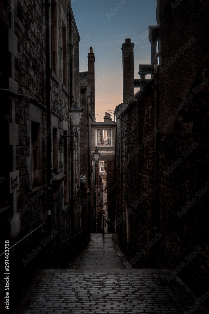 Narrow European alley, surrounded by bricks and cobblestone. Illuminated only with weak light from sunrise. Concept of scared or being alone and frightened