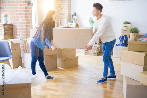 Beautiful young asian couple looking happy, holding a big cardboard box smiling excited moving to a new home