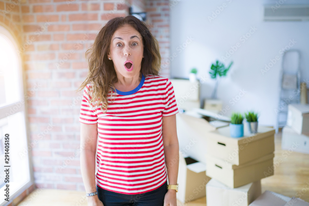 Middle age senior woman moving to a new house packing cardboard boxes afraid and shocked with surprise expression, fear and excited face.