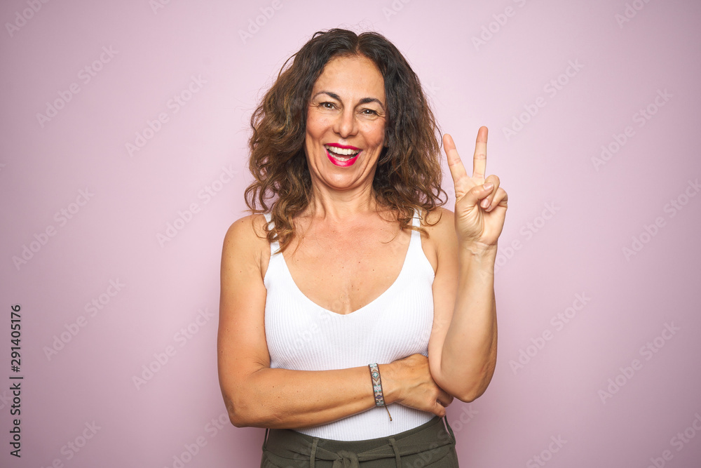Middle age senior woman standing over pink isolated background smiling with happy face winking at the camera doing victory sign. Number two. Middle age senior woman standing over pink isolated background smiling with happy face winking at the camera doing victory sign. Number two.