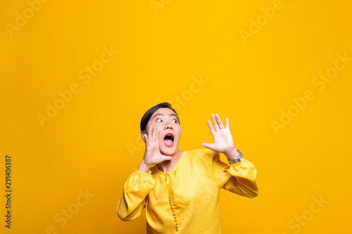Happy woman making shout gesture isolated over yellow background