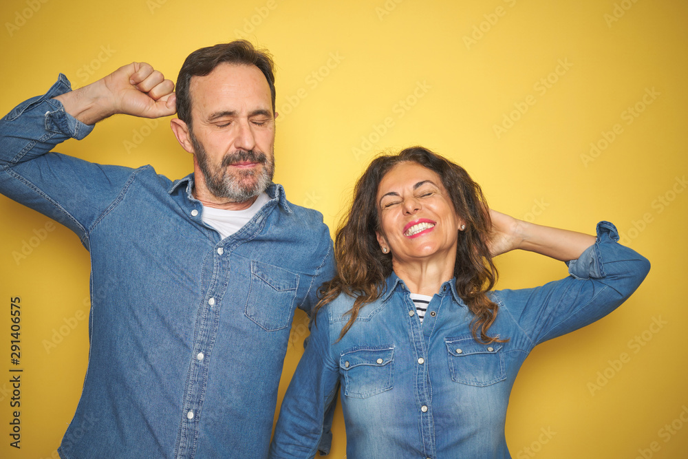 Obraz premium Beautiful middle age couple together standing over isolated yellow background stretching back, tired and relaxed, sleepy and yawning for early morning