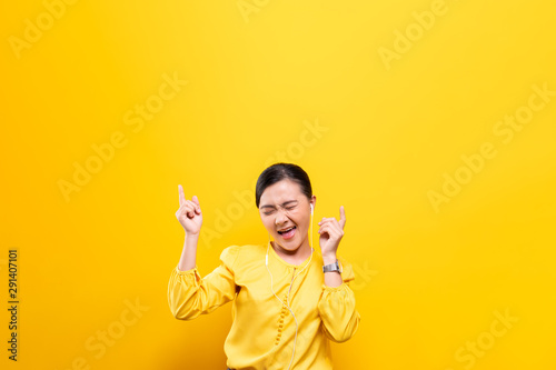 Woman with earphones listening music on isolated yellow background