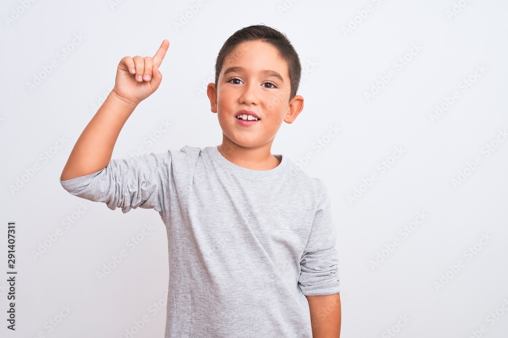 Beautiful kid boy wearing grey casual t-shirt standing over isolated white background pointing finger up with successful idea. Exited and happy. Number one.