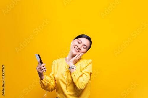 Woman with earphones listening music from smartphone on isolated yellow background