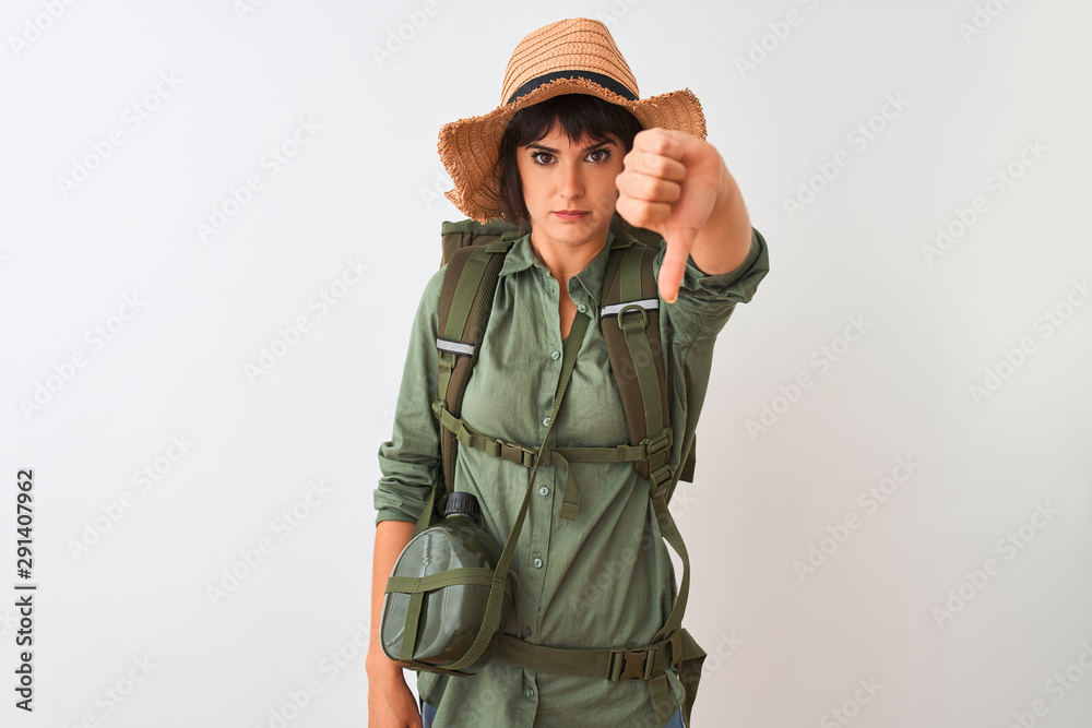 Hiker woman wearing backpack hat and water canteen over isolated white background looking unhappy and angry showing rejection and negative with thumbs down gesture. Bad expression.