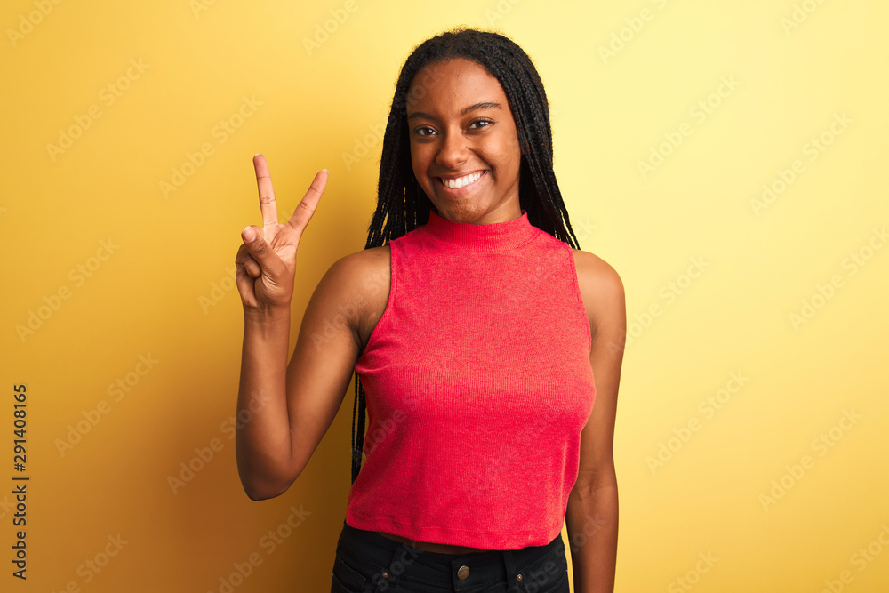 African american woman wearing red casual t-shirt standing over isolated yellow background showing and pointing up with fingers number two while smiling confident and happy. African american woman wearing red casual t-shirt standing over isolated yellow background showing and pointing up with fingers number two while smiling confident and happy.