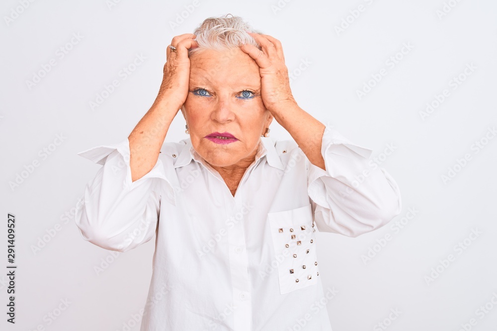 Senior grey-haired woman wearing elegant shirt standing over isolated white background suffering from headache desperate and stressed because pain and migraine. Hands on head. Senior grey-haired woman wearing elegant shirt standing over isolated white background suffering from headache desperate and stressed because pain and migraine. Hands on head.