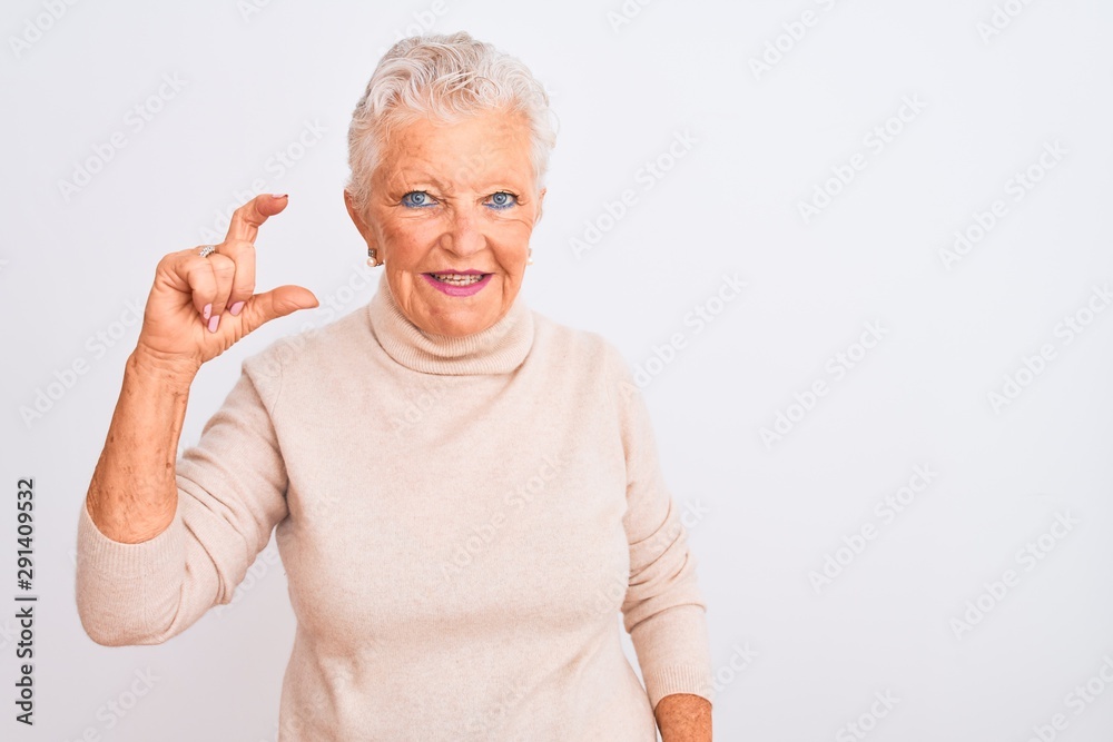 Senior grey-haired woman wearing turtleneck sweater standing over isolated white background smiling and confident gesturing with hand doing small size sign with fingers looking and the camera Senior grey-haired woman wearing turtleneck sweater standing over isolated white background smiling and confident gesturing with hand doing small size sign with fingers looking and the camera