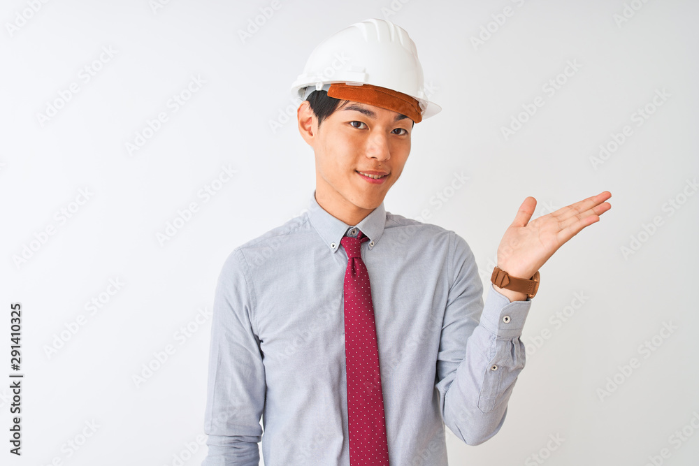 Chinese architect man wearing tie and helmet standing over isolated white background smiling cheerful presenting and pointing with palm of hand looking at the camera.