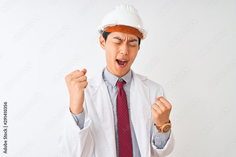 Chinese architect man wearing coat and helmet standing over isolated white background very happy and excited doing winner gesture with arms raised, smiling and screaming for success Chinese architect man wearing coat and helmet standing over isolated white background very happy and excited doing winner gesture with arms raised, smiling and screaming for success