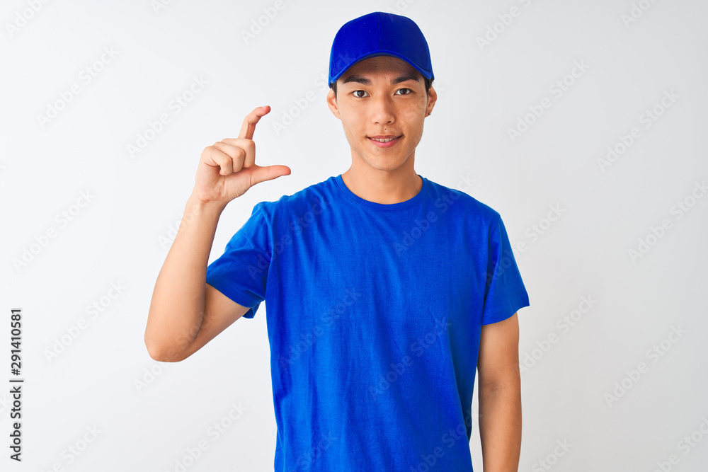 Chinese deliveryman wearing blue t-shirt and cap standing over isolated white background smiling and confident gesturing with hand doing small size sign with fingers looking and the camera Chinese deliveryman wearing blue t-shirt and cap standing over isolated white background smiling and confident gesturing with hand doing small size sign with fingers looking and the camera
