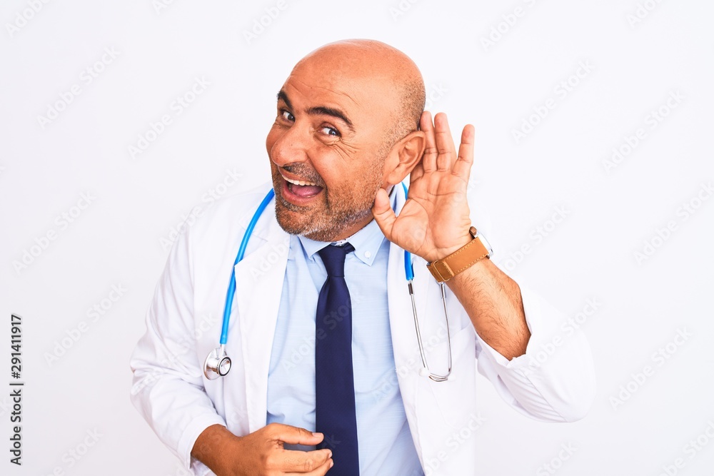 Middle age doctor man wearing stethoscope and tie standing over isolated white background smiling with hand over ear listening an hearing to rumor or gossip. Deafness concept. Middle age doctor man wearing stethoscope and tie standing over isolated white background smiling with hand over ear listening an hearing to rumor or gossip. Deafness concept.
