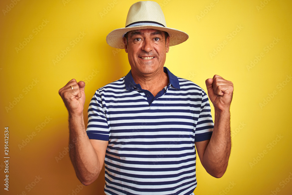Handsome middle age man wearing striped polo and hat over isolated yellow background celebrating surprised and amazed for success with arms raised and open eyes. Winner concept. Handsome middle age man wearing striped polo and hat over isolated yellow background celebrating surprised and amazed for success with arms raised and open eyes. Winner concept.
