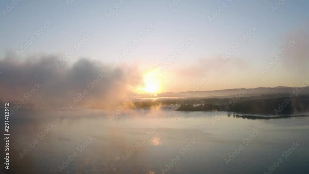 Sunrise at a lake, flying through a mist floating over a water surface.