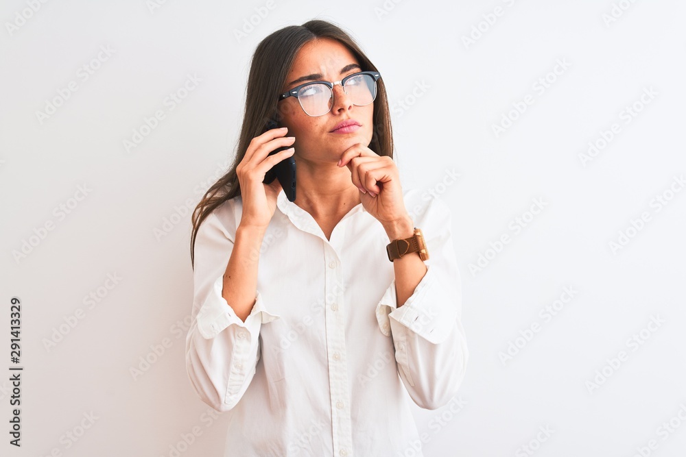 Young businesswoman wearing glasses talking on smartphone over isolated white background serious face thinking about question, very confused idea Young businesswoman wearing glasses talking on smartphone over isolated white background serious face thinking about question, very confused idea