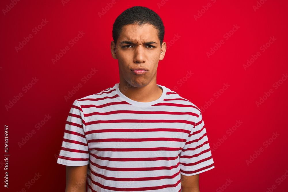 Young handsome arab man wearing striped t-shirt over isolated red background skeptic and nervous, frowning upset because of problem. Negative person. Young handsome arab man wearing striped t-shirt over isolated red background skeptic and nervous, frowning upset because of problem. Negative person.