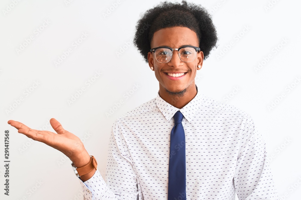 Young african american businessman wearing tie and glasses over isolated white background smiling cheerful presenting and pointing with palm of hand looking at the camera. Young african american businessman wearing tie and glasses over isolated white background smiling cheerful presenting and pointing with palm of hand looking at the camera.