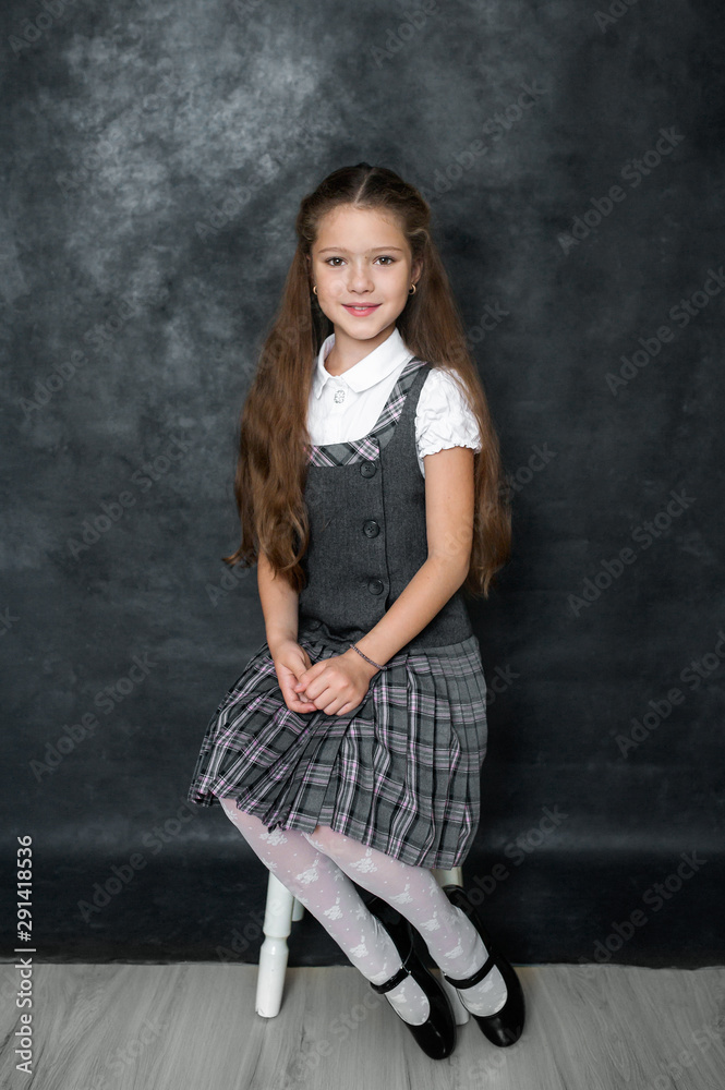 Naklejka premium Portrait of a cute little kid girl on a gray background. Child schoolgirl looking at the camera. The concept of education. Copy space.