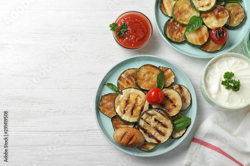 Flat lay composition with delicious grilled zucchini slices on white wooden table. Space for text
