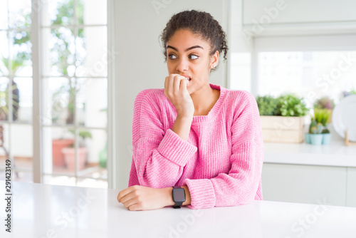 Beautiful african american woman with afro hair wearing casual pink sweater looking stressed and nervous with hands on mouth biting nails. Anxiety problem.