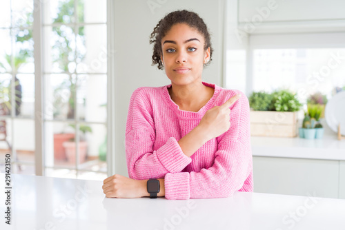 Free Download Beautiful african american woman with afro hair wearing casual pink sweater Pointing with hand finger to the side showing advertisement, serious and calm face - GFXLoad
