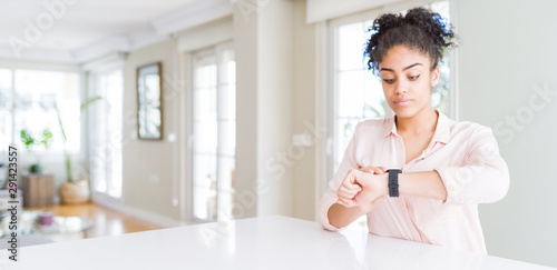 Wide angle of beautiful african american woman with afro hair Checking the time on wrist watch  relaxed and confident