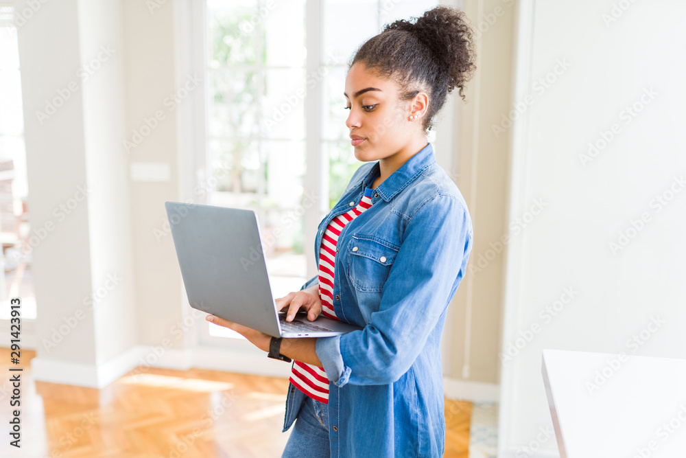 Young african american girl standing working using laptop with a confident expression on smart face thinking serious Young african american girl standing working using laptop with a confident expression on smart face thinking serious