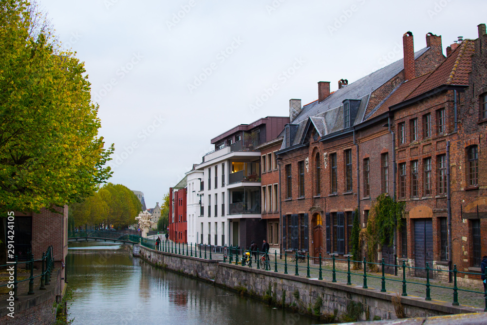 Naklejka premium Typical belgian street in Patershol in the coastline of Lys river and a bridge at the background, with houses and trees