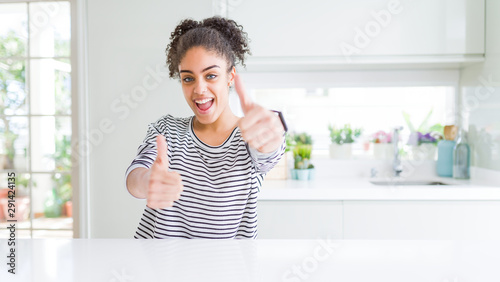 Beautiful african american woman with afro hair wearing casual striped sweater approving doing positive gesture with hand  thumbs up smiling and happy for success. Winner gesture.