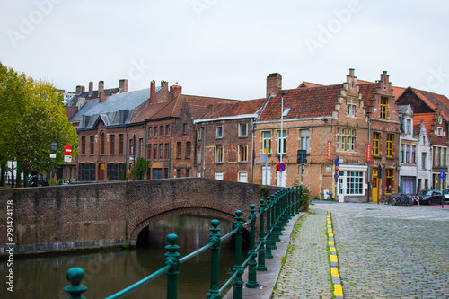 Ghent, Belgium; 10/29/2018: Typical belgian street in Patershol with green railings, Lys river and a brick bridge at the background, with houses and trees photo